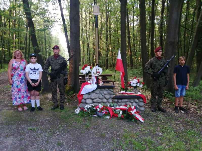 Pamiątkowe zdjęcie Oliwiera Morończyka, Patrycji Dziadek oraz nauczycielki historii Renaty Martyniak pod pomnikiem wraz z żółnierzami pełniącymi wartę honorową